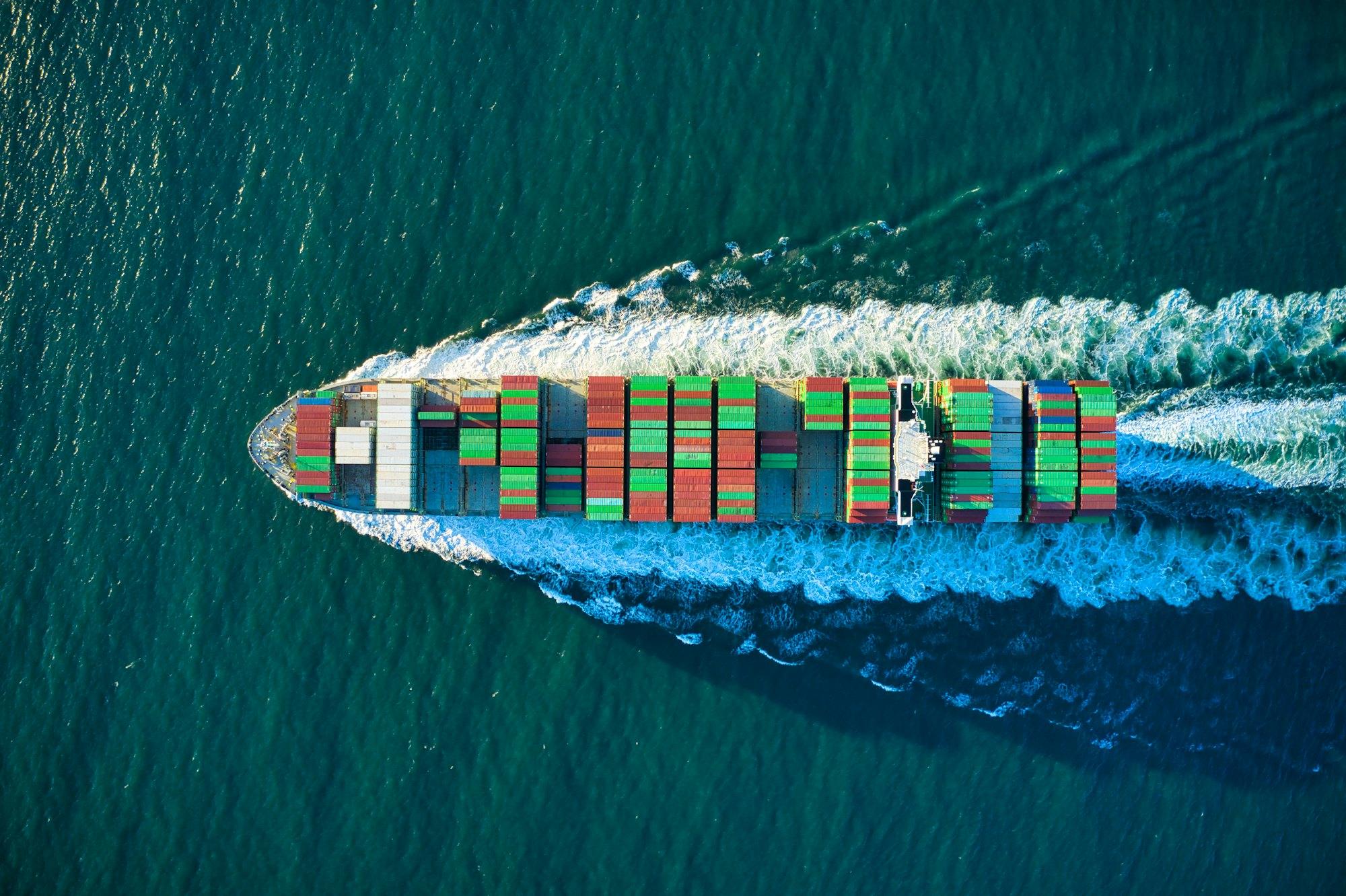 Aerial view of a loaded container ship cutting through dark teal water